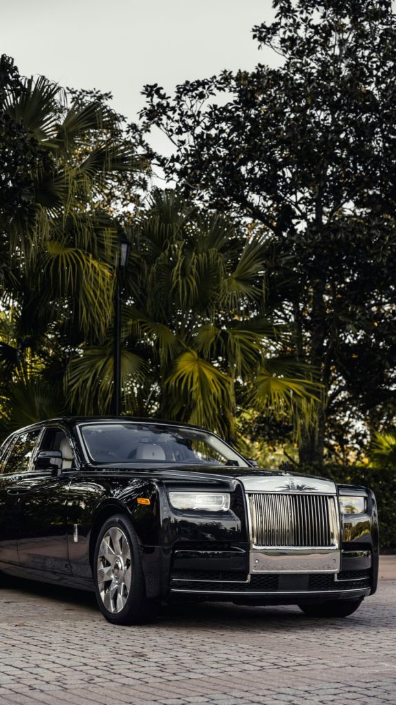 a black rolls royce parked in front of some trees